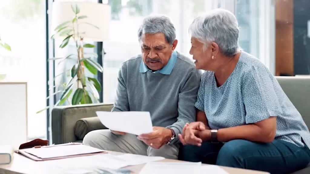 Older couple on a sofa reading through paperwork together.