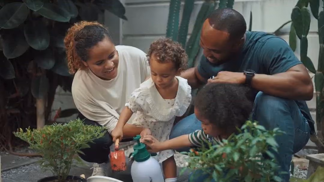 Parents and their young children watering plants together in a garden.
