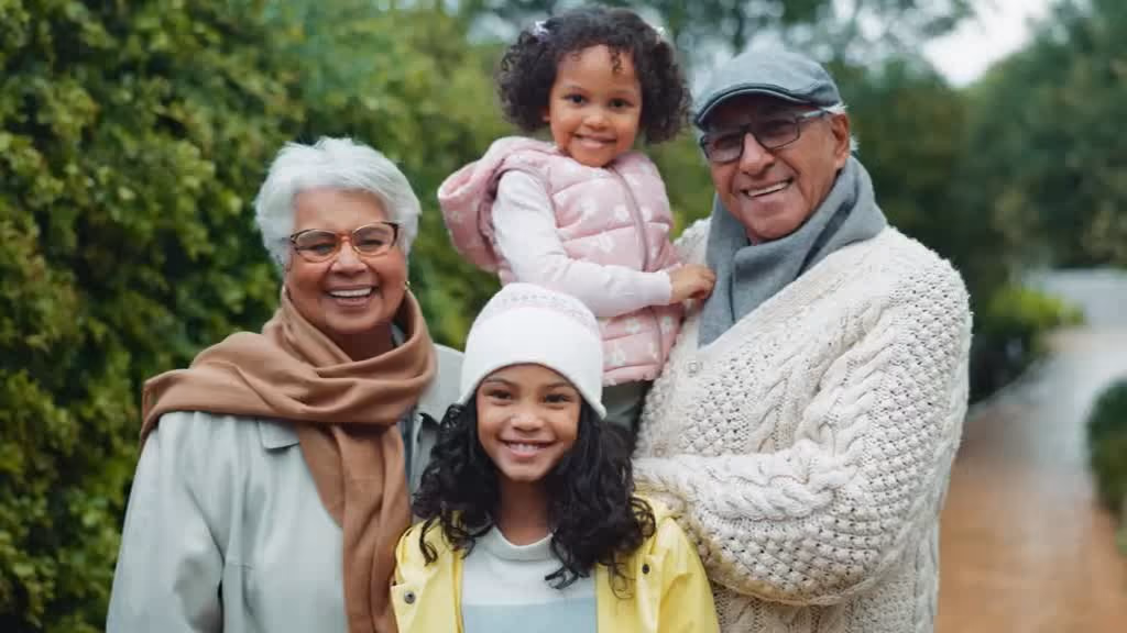 Grandparents outdoors with their two granddaughters, smiling together.