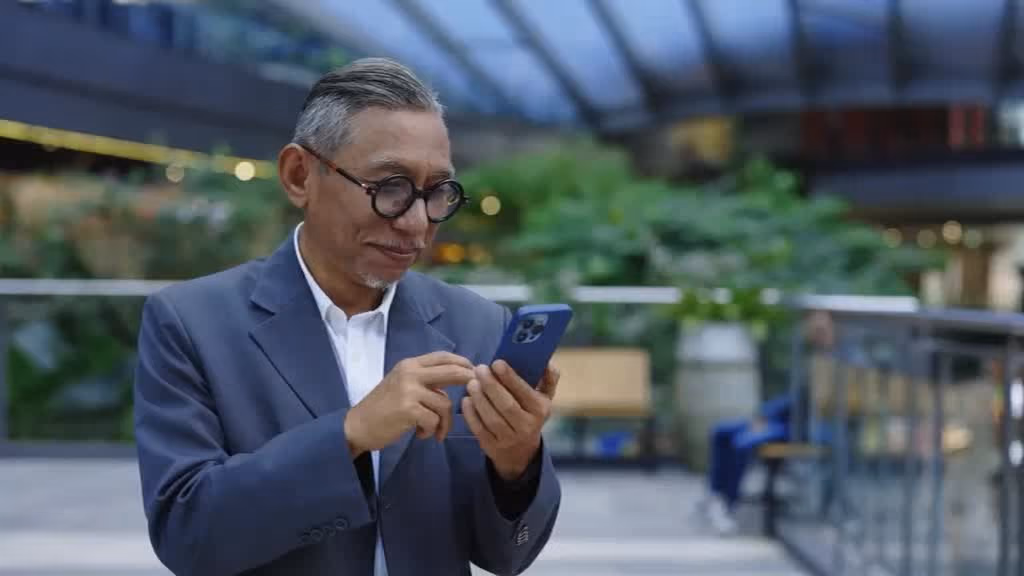 Man in a suit checking his phone in a bright office atrium.